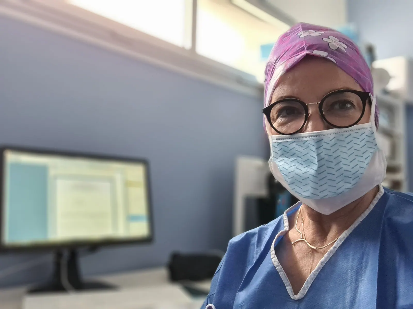 Le Dr Joëlle Huth au bloc opératoire, en tenue chirurgicale, charlotte fleurie et lunettes