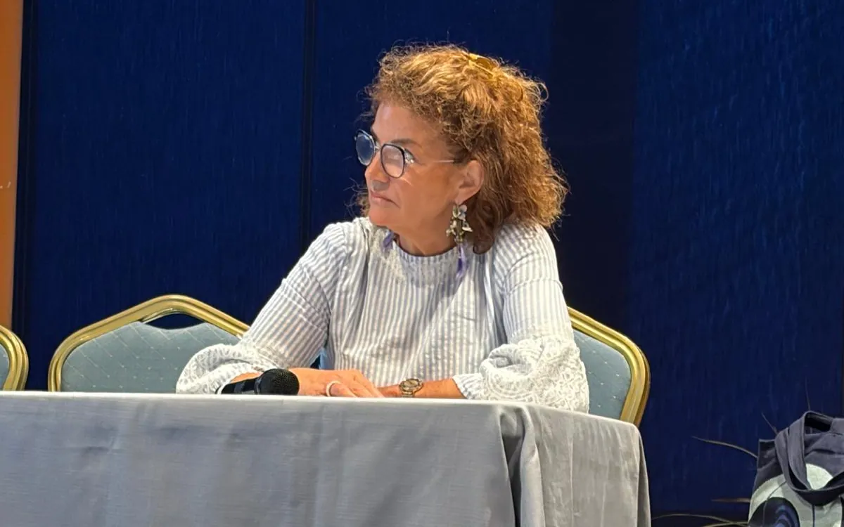 Le Dr Joëlle Huth assise à la table d’un congrès, un micro devant elle, regardant sur le côté