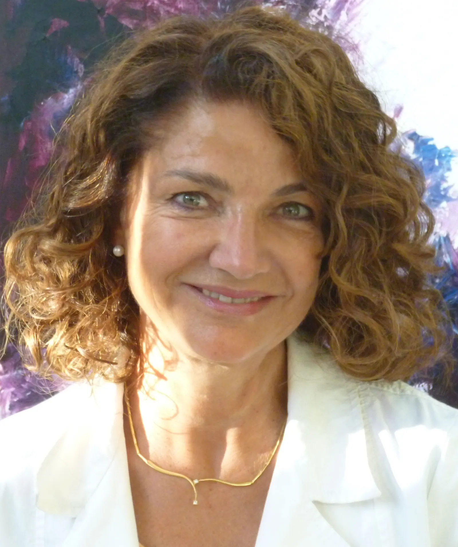 Portrait du Dr Joëlle Huth, souriante, en blouse blanche devant une toile aux teintes violettes et bleues